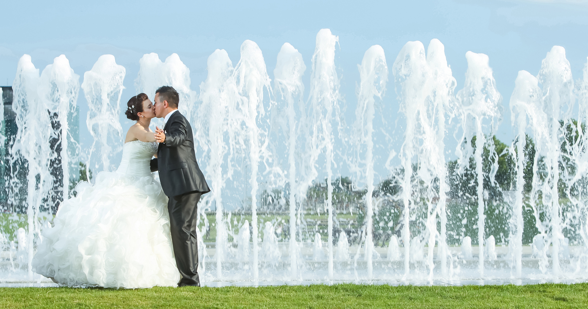 Bride and groom kissing in front of water spray fountain