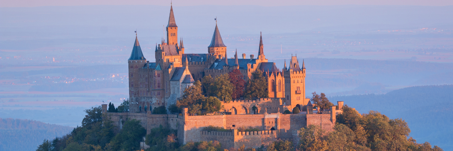 A majestic castle perched atop a mountain, surrounded by a clear blue sky and distant hills.