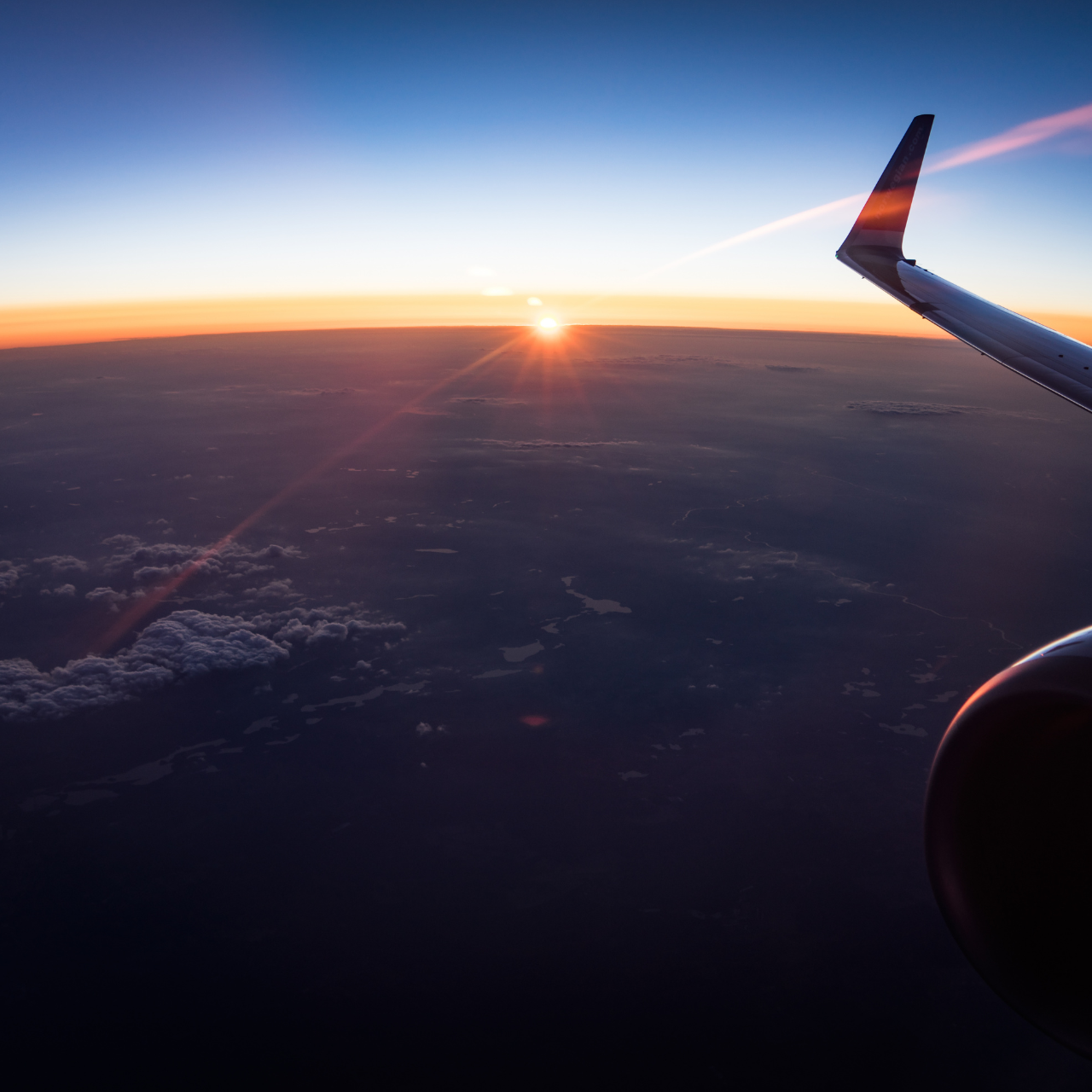 A breathtaking sunset view from an airplane window, showcasing vibrant hues of orange, pink, and purple in the sky.